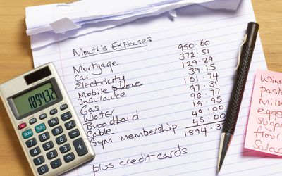 An image of a calculator, pen and paper with the list of bills.